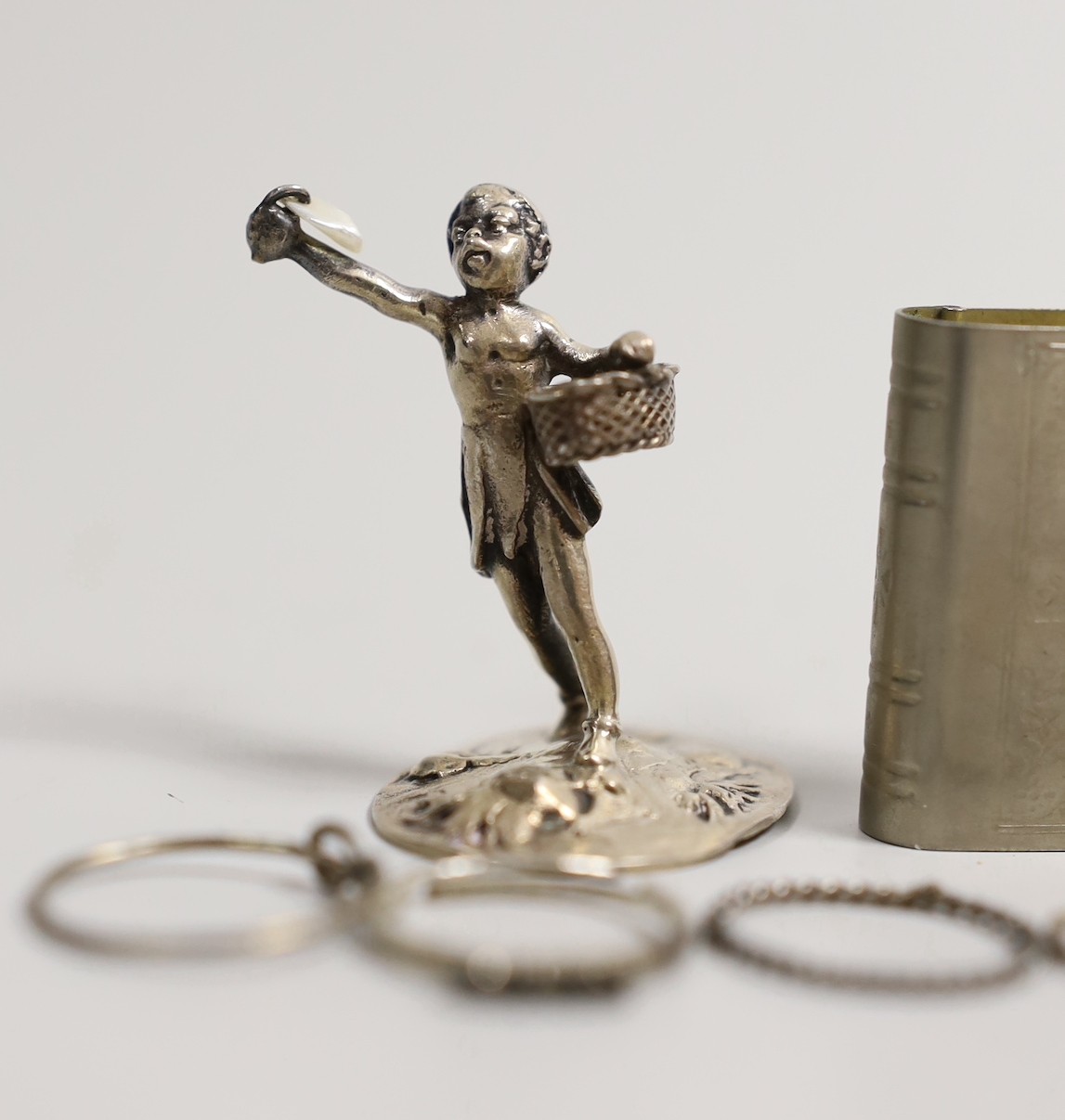 An Edwardian silver miniature model of an occasional chair, import marks for London, 1902, 43mm, a continental white metal model of a shoe and a similar model of a young child, a base metal 'book' box containing a rosary